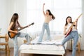 Happy group of Asian friends singing and jumping on bed at home. Cheerful Asia women have fun together playing guitar with melody Royalty Free Stock Photo