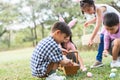 Happy group of diverse cute children hunting Easter eggs, girl wearing bunny ears. kids holding basket, picking eggs on grass Royalty Free Stock Photo