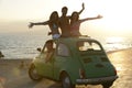 Happy group of friends with small car on beach