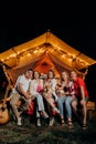 Happy group of friends with Welsh Corgi Pembroke dogs relaxing in glamping on summer evening near cozy bonfire. Luxury camping