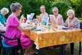 Happy group of senior ladies enjoying art class seated around a table outdoors in the garden painting with water colors while