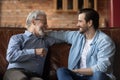 Happy grown son and older father resting on couch