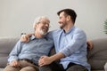 Happy grown son sit on couch talk with senior dad