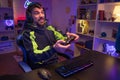 Happy guy gamer wear headphone play video game colorful neon lights computer in living room.