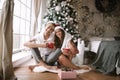 Happy guy and girl in white t-shirts and Santa Claus hats sit with red cups on the floor in front of the window next to Royalty Free Stock Photo