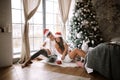 Happy guy and girl in white t-shirts and Santa Claus hats are sitting and hugging in the room on the floor in front of Royalty Free Stock Photo