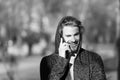 Happy guy in hood talk on mobile phone on sunny outdoor. Bearded man smile in hood on fresh air. Fashion macho smiling Royalty Free Stock Photo