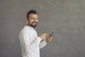 Happy young man using mobile phone standing isolated on grey copy space background Royalty Free Stock Photo