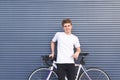 Happy guy in a white T-shirt standing with a white bike against the wall, looking at the camera and smiling Royalty Free Stock Photo