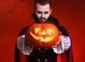 Happy Halloween! bearded man in a Dracula vampire costume with a pumpkin on a glowing red background