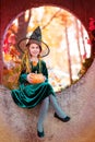 Happy halloween celebration. Beautiful girl witch with pumpkin in the park, outdoors