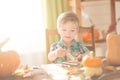 Happy Halloween concept. Cute little happy boy carving a pumpkin and decorated cookies for halloween on table indoors. Royalty Free Stock Photo