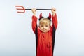 Happy Halloween! Cute little boy in devil halloween costume with horns and trident on light blue background Royalty Free Stock Photo