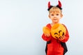 Happy Halloween! Cute little boy in devil halloween costume with pumpkin basket jack-o-lantern on light blue background Royalty Free Stock Photo