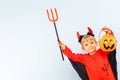 Happy Halloween! Cute little boy in devil halloween costume with trident and pumpkin basket jack-o-lantern on light blue Royalty Free Stock Photo