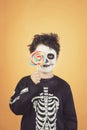 Happy Halloween.funny child in a skeleton costume covering eye with lollipop