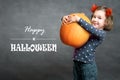 Happy Halloween! Funny little girl holds big pumpkin and smiles. Adorable child and Halloween typography Royalty Free Stock Photo