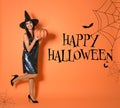 Happy Halloween greeting card design. Woman wearing witch costume with pumpkin on orange background