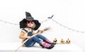 Happy Halloween: A little girl sits on a table in a witch hat with a broom. Royalty Free Stock Photo