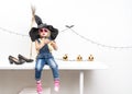 Happy Halloween: A little girl sits on a table in a witch hat with a broom. Royalty Free Stock Photo