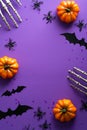 Happy Halloween poster mockup. Flat lay bony hands, pumpkins, bats silhouettes on purple background. Top view with copy space