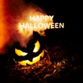 Happy Halloween text glowing in red and yellow smoke at night above a creepy pumpkin Jack o Lantern