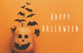 Happy Halloween text, greeting card. Pumpkin with face and black bats, ghost, spider paper decorations on orange background. Flat Royalty Free Stock Photo