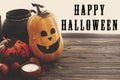 Happy Halloween text sign on pumpkins, jack-o-lantern, witch cauldron, bats, spider, candle, autumn leaves on black wood in light Royalty Free Stock Photo