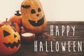 Happy Halloween text sign on pumpkins, jack-o-lantern, witch cauldron, bats, spider, candle, autumn leaves on black wood in light Royalty Free Stock Photo