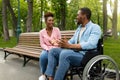 Happy handicapped black guy in wheelchair talking to his girlfriend at park, copy space