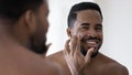 Happy handsome African American man applying moisturizer on face