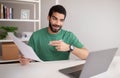 Happy handsome arab man in green t-shirt point fingers at documents, has video call