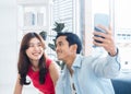 Happy handsome Asian man and young beautiful woman selfie while sitting near the glass window. Royalty Free Stock Photo