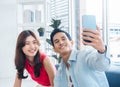 Happy handsome Asian man and young beautiful woman selfie while sitting near the glass window at white living room. Royalty Free Stock Photo