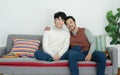 Happy handsome Asian young gay couple wearing sweater embracing his boyfriend looking at camera and sitting on sofa at home Royalty Free Stock Photo