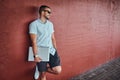 Happy handsome fashionable freelancer in sunglasses dressed in a white shirt and shorts holds a laptop computer standing