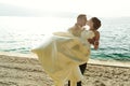 Happy handsome groom holding bride in his arms on beach at sunset Royalty Free Stock Photo
