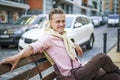 Happy and handsome individual with lazy and carefree expression, smiling while sitting on bench in urban city