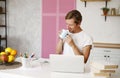 Happy handsome man reviewing his lesson with laptop sitting in kitchen drinking tea or coffee. Online education or freelance Royalty Free Stock Photo