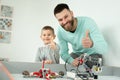 Happy handsome man smiles at the camera with his cheerful little son while playing with lego robots and shows the thumbs Royalty Free Stock Photo