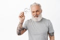 Happy handsome mature man with beard and tattoos, take off glasses and wink cheeky and confident at camera, standing in Royalty Free Stock Photo