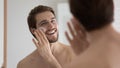 Happy handsome metrosexual guy applying sunscreen on face at mirror Royalty Free Stock Photo