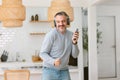 Happy handsome middle age man with wireless headphones listening to the music with smartphone, dancing and smiling at home in cozy Royalty Free Stock Photo