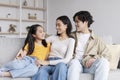 Happy handsome millennial asian couple watching at teen daughter, hugging, sitting on sofa in living room