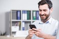 Happy handsome office worker sitting at a computer desk in the office using a mobile phone. Cheerful bearded business man Royalty Free Stock Photo