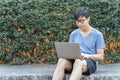 Happy handsome young Asian business man in casual clothes is using laptop to check his business, work and social media in outdoor Royalty Free Stock Photo