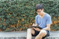 Happy handsome young Asian business man in casual clothes is using tablet to check his business, work and social media in garden Royalty Free Stock Photo