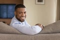 Happy handsome young Black homeowner man sitting on couch Royalty Free Stock Photo