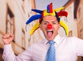 Happy handsome young businessman with a red clown nose and colorful harlequin hut in his head Royalty Free Stock Photo