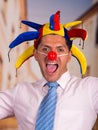 Happy handsome young businessman with a red clown nose and colorful harlequin hut in his head Royalty Free Stock Photo